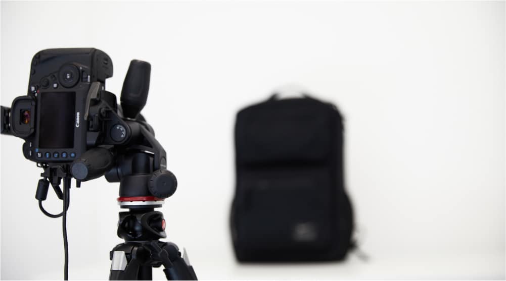 A camera with a tripod and a backpack in front of it.